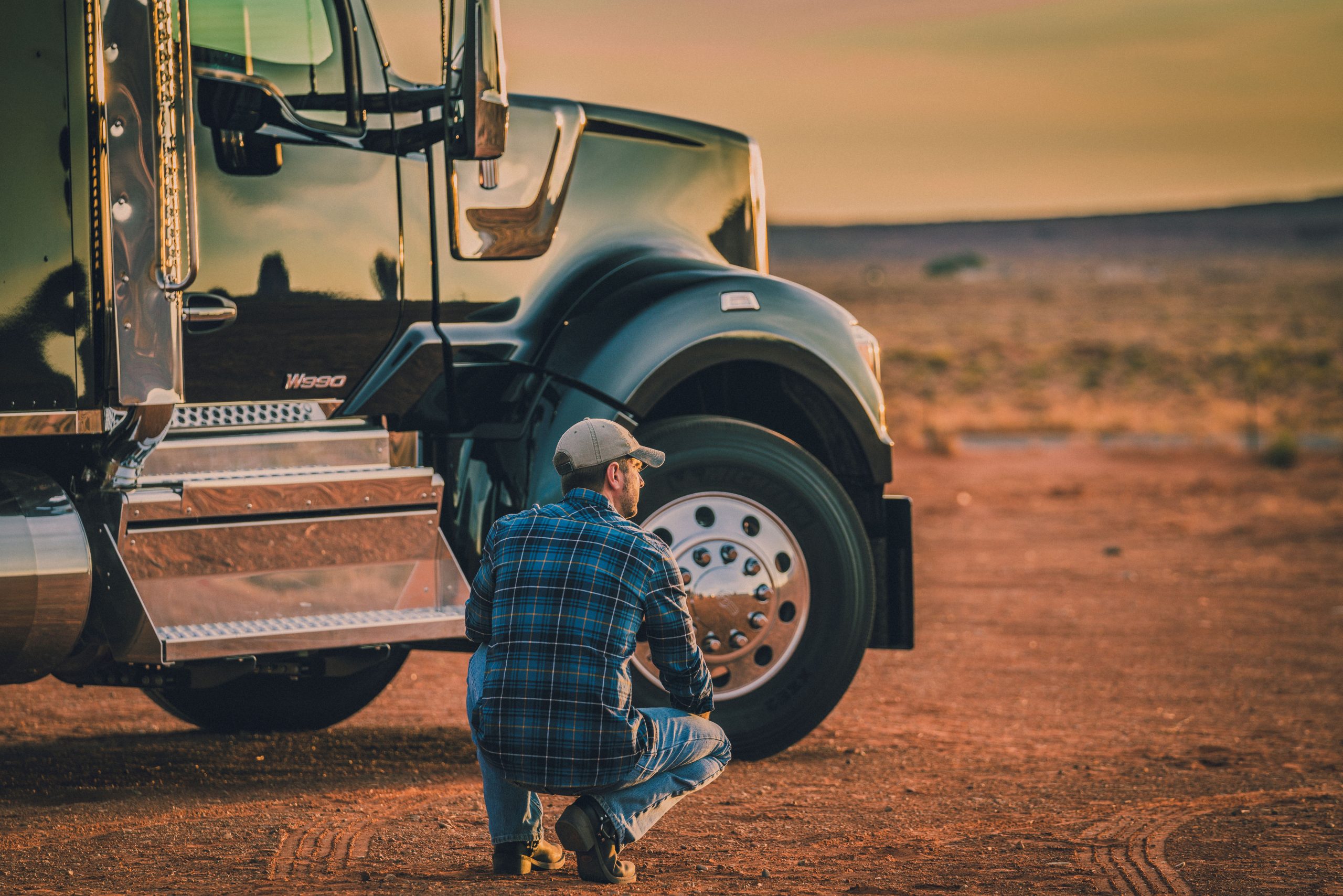 Man hunched down next to a Kenworth Truck. DOT Physical Requirements.